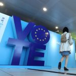 A woman walks past an advertising board for the EU elections at the Schuman railway station near the European Parliament in Brussels
